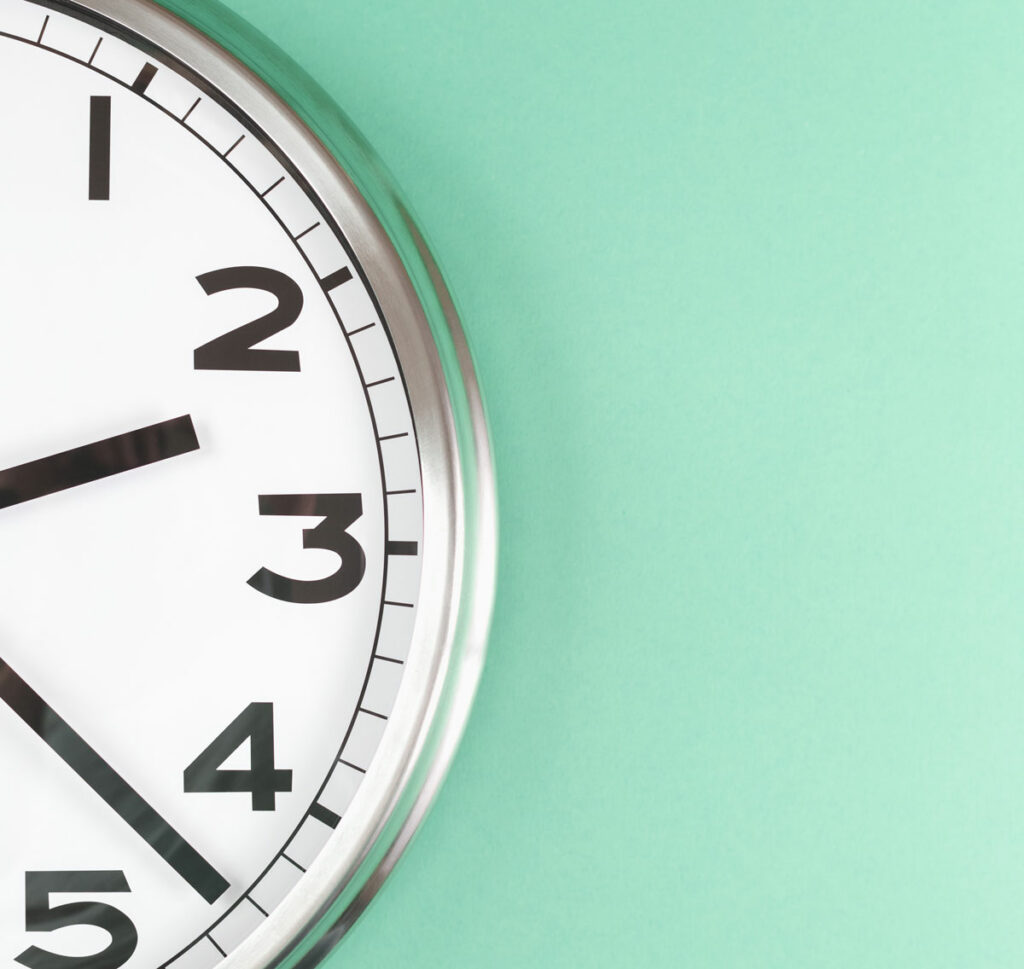 Wanduhr mit schwarzem Ziffernblatt und silbernem Gehäuse vor mintgrünem Hintergrund. Die Uhr zeigt kurz nach drei Uhr. Ideal für zeitbezogene Themen und Raumgestaltung.